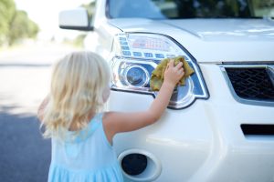 A young girl helping to wash a car outside.