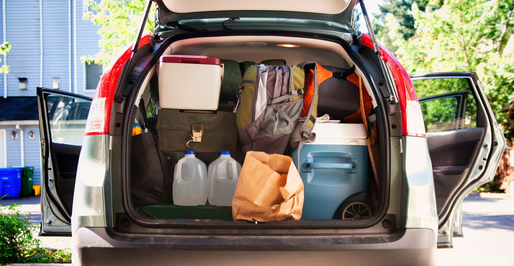 A car trunk packed with essential tailgate supplies, including coolers, bags, and water jugs, ready for a game day event.