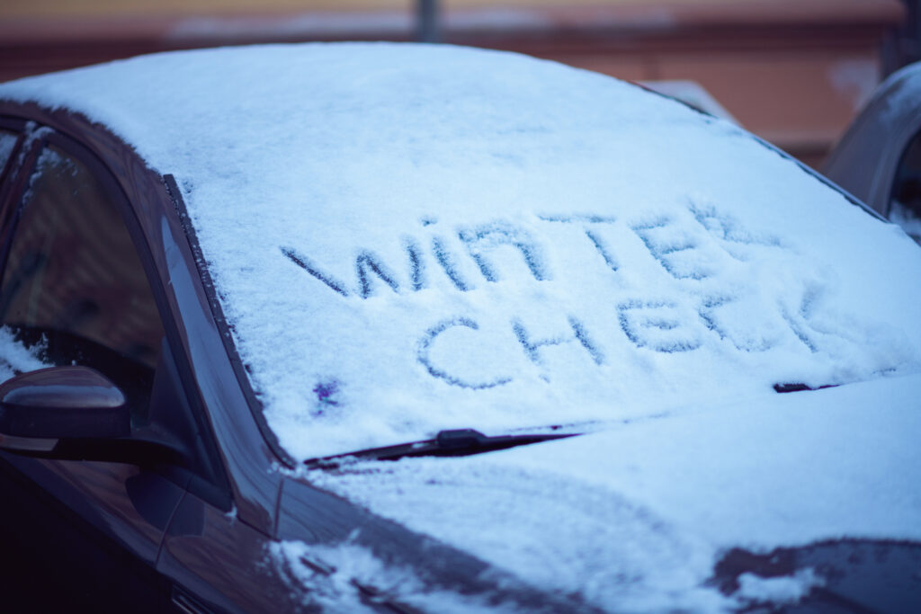 Car windshield covered in snow with 'Winter Check' written on it.