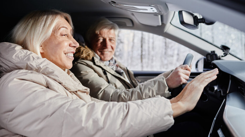 Older couple warming up inside a car during winter, adjusting the car’s heater.