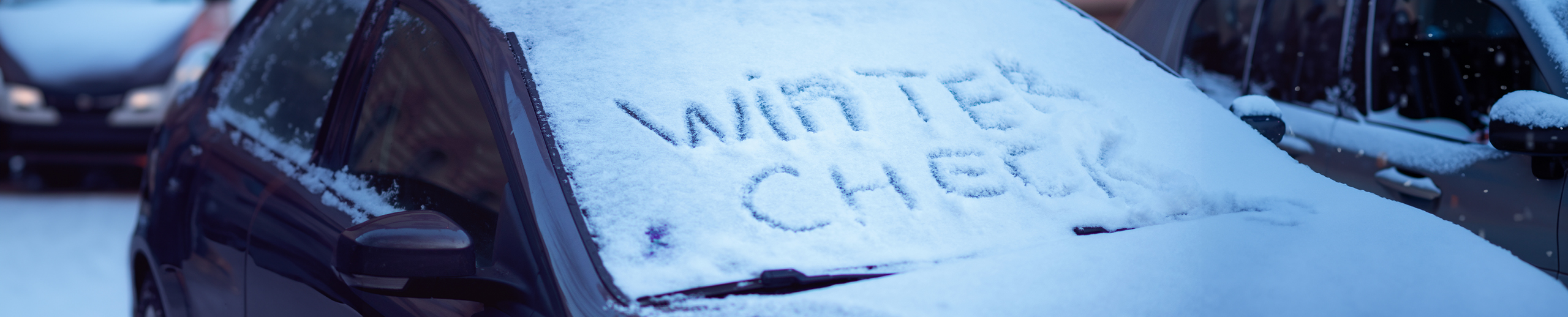 Car windshield covered in snow with 'Winter Check' written on it.