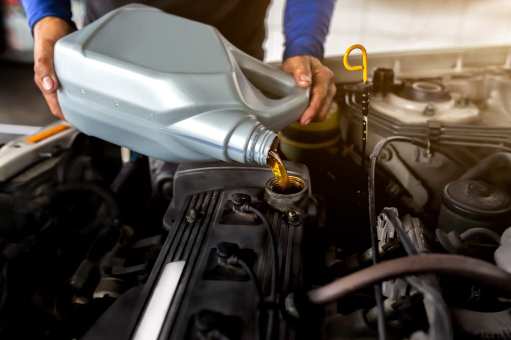 A close-up of a person pouring fresh motor oil into a car engine, demonstrating the importance of regular oil changes for spring vehicle maintenance.